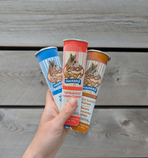 Three yogurt tubes with different flavors held by a hand on a wooden surface