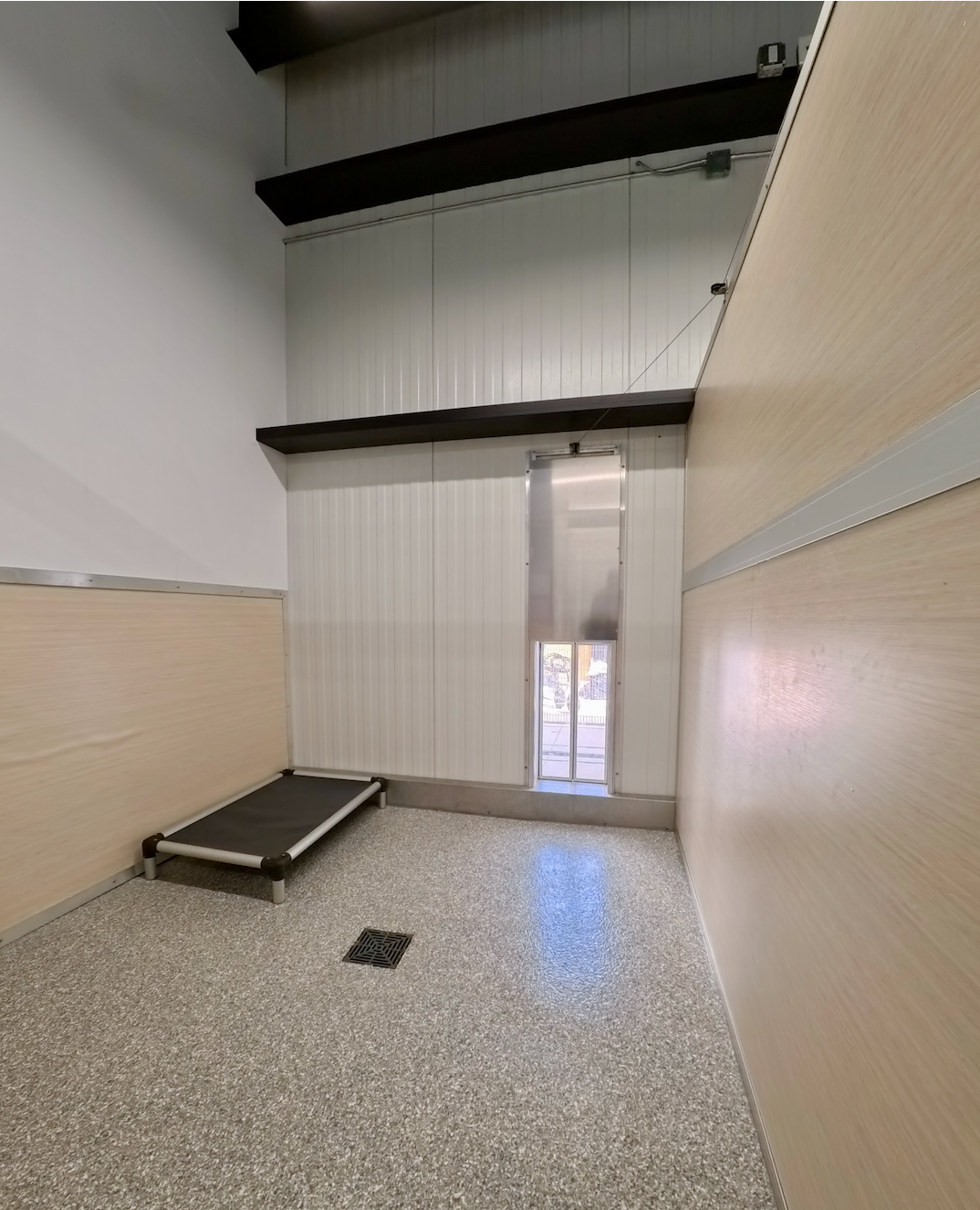 Inside of a villa kennel with dog bed and doggy door to outside patio